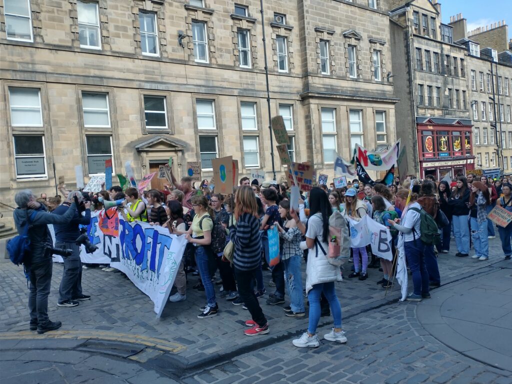 Climate strikers in Edinburgh's High Street, 25 March 2022. Big crowd of mainly young people on road behind PEOPLE NOT PROFIT banner